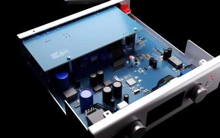 Pohľad zhora a zľava na strieborný hliníkový elektronický box s odstráneným krytom, odhaľujúci matne modrú dosku plošných spojov s modrými a čiernymi valcovými kondenzátormi, čiernym predným displejom a dvoma veľkými zladenými ovládacími kolieskami