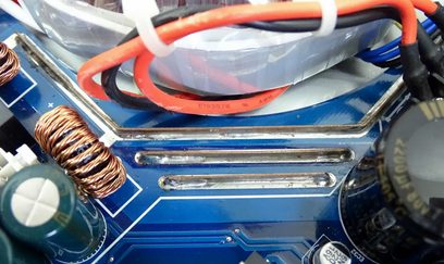 Modrá základní deska počítače s elektronickými součástkami, oranžovými kabely a stříbrným kovovým chladičem
