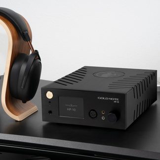 Auriculares negros sobre soporte de madera curvada, amplificador negro Gold Note HP-10 con pantalla, botones y conectores en el panel frontal