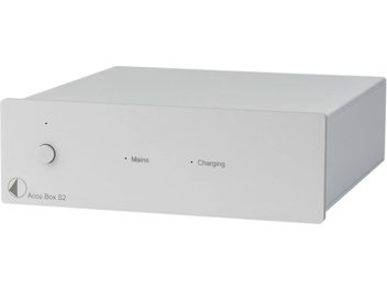 Erillinen virtalähde HI-FI-elektroniikalle Accu Box S2, hopeanvärinen suorakaiteen muotoinen metallikotelo, pyöreä painike vasemmalla, kaksi merkkivaloa ja etupaneelissa tekstit "Mains" ja "Charging", hieman vinosta kulmasta otettu perspektiivikuva.