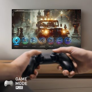 Fladskærm på væggen viser et videospil med køretøj, hænder holder en sort controller i forgrunden, tekst "Game Mode Plus"