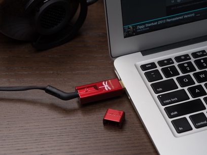 USB-lydkonverter Audioquest DragonFly Red, rød USB-nøgle tilsluttet en sølvfarvet bærbar computer, tæt på-billede