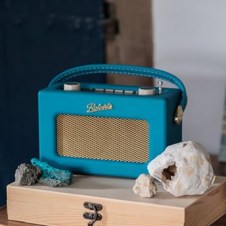 Bærbar retro turkis radio i kunstlæder, set fra tre kvart forfra, med forsidegitter i gyldent metal, matchende håndtag øverst og to store drejeknapper på toppen