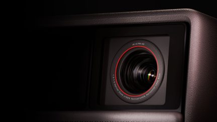 Juodo metalo ir stiklo projektoriaus objektyvas su raudonu žiedu ir 4K Ultra HD žymėjimu, artimas vaizdas iš priekio