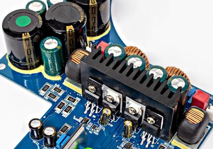 Placă de circuit imprimat albastră, radiator din aluminiu negru, condensatoare verzi și negre, bobine din cupru, vedere macro oblică
