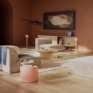 Stue med beige sofa, glas sofabord, lyserød skammel, lyst tæppe, hvid væghylde, sort hængelampe