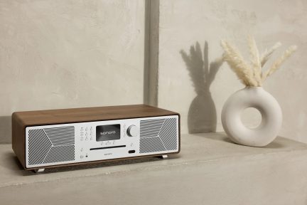 Radio Sonoro Meisterstück (gen 2) i valnød og sølv finish, 3/4 visning, placeret på en beige overflade, hvid cirkulær vase