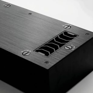 Enceinte encastrable murale PMC Ci140, vue de dessus, grille noire avec logo, fixations apparentes sur plaque métallique brossée