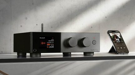 Amplificador estéreo audiolab preto com ecrã a cores, dois grandes botões rotativos, smartphone em emparelhamento de áudio Bluetooth