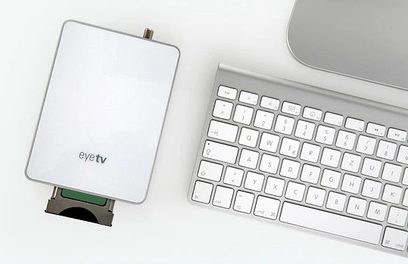 Teclado de ordenador blanco y caja TV Elgato EyeTV Sat negra con conector USB, sobre fondo gris claro