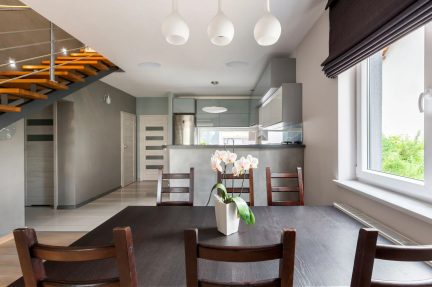 Modernes Esszimmer mit großem dunklem Tisch, Stühlen mit durchbrochenen Rückenlehnen, Orchidee und offener grauer Küche