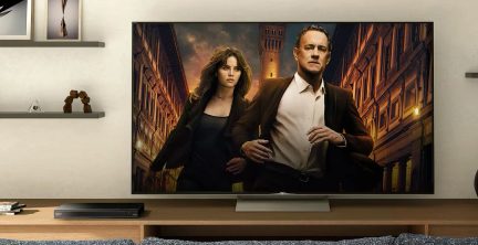 Fladskærms-tv på træmøbel, billede af to personer i mørkt tøj, bygninger i baggrunden