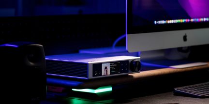 Case audio hi-fi rettangolare in alluminio argentato spazzolato, vista tre quarti anteriore, pannello laterale con feritoie di ventilazione, frontale nero con schermo a colori, presa cuffie e grande manopola nera