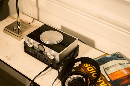 sølvfarvet hi-fi hovedtelefonforstærker med store runde knapper, kablede hovedtelefoner lagt ved siden af på marmorbord
