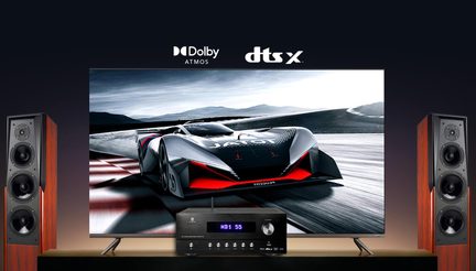 Dolby Atmos dtsX hjemmebiografsæt med tv, der viser racerbilen, sort AV-forstærker og to gulvhøjttalere i træ