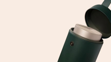 Nærbillede af en åben grøn cylindrisk kasse, der indeholder en sølvfarvet metalgenstand med riller på toppen