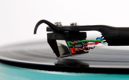 Black turntable arm with cartridge, colored wires, black vinyl record, close-up side view