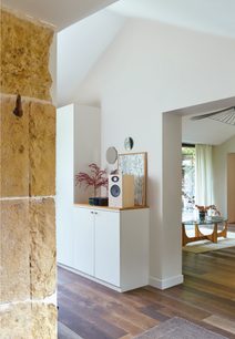 Enceinte bibliothèque Focal Theva N°1 chêne clair, en bois clair, sur meuble blanc, dans pièce avec mur en pierre