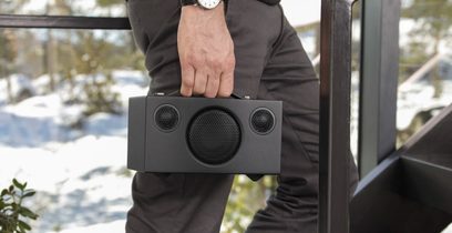 Sort bærbar højttaler Audio Pro ADDON C3 holdt i en mands hånd iført mørk grå jakkesæt, tæt forfra-perspektiv