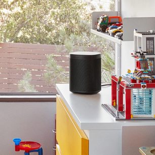Trådløs tilsluttet Sonos One (Gen 2) højttaler i mat sort, cylindrisk form, på hvid hylde med farverige Lego-legetøj