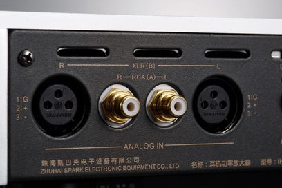 Primo piano frontale sui connettori XLR a tre poli neri e RCA dorati incassati in un pannello posteriore in metallo nero opaco con bordo in alluminio argento del preamplificatore per cuffie Cayin IHA-8 argento