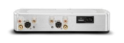 Vista trasera de una caja de audio rectangular de aluminio cepillado plateado, equipada con terminales de altavoz transparentes, dos conectores XLR negros, tomas RCA doradas, una entrada mini-jack de disparo y un bloque de alimentación IEC con interruptor basculante integrado
