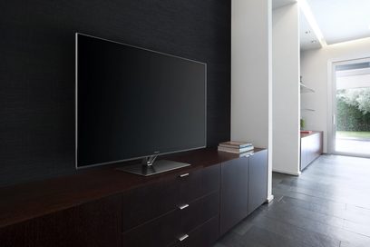 Sort fladskærms-tv stående på et mørkt trækabinet i et hvidt rum med en glasvæg til højre