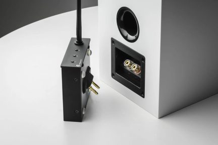 Weiße Regallautsprecher-Rückansicht mit Bassreflexöffnung, Anschlussklemmen und schwarzem kabellosem Audio-Adapter mit Antenne