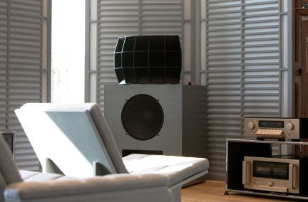 Grote grijze hi-fi-luidspreker met zwarte hoorn, audioversterker op een meubel in een luisterkamer