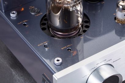Nærbilde i lett fugleperspektiv av Cayin Jazz 100 rørforsterker i svart, med glitrende svart metallchassis og børstet sølvfarget aluminiumsfront, som fremhever 805A-glassrøret omgitt av sirkulære perforeringer, en bias-justeringsbryter og en stor sylindrisk volumknapp.
