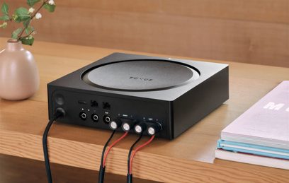 Ampli hi-fi stéréo Sonos Amp noir, vue de face, connecteurs à l'arrière, bouton rotatif sur le dessus, posé sur une table en bois
