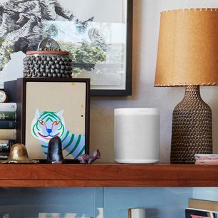 Trådløs tilsluttet Sonos One (Gen 2) højttaler i mat hvid, lampe, ramme med stiliseret tiger, bøger og dekorative genstande på træhylde