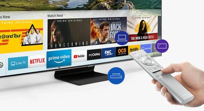 Bílý dálkový ovladač s tlačítky namířený na televizní obrazovku zobrazující náhledy streamovacích programů