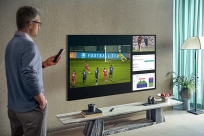 Samsung QE85QN800A-fladskærm, der viser en fodboldkamp, stående på et lyst træmøbel i en stue