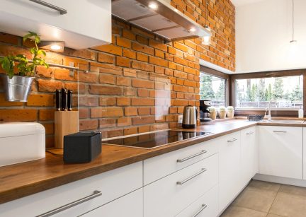 White modern corner kitchen with wooden worktop, brick wall and black induction hob