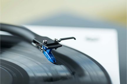 Modrá buňka s černým ramenem a kovovými šrouby na černé vinylové desce, detailní pohled v mírném úhlu