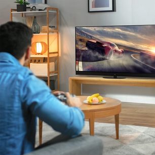Panasonic TX-48JZ980E-fladskærms-tv, der viser et rødt racerbil på en racerbane, set bagfra foran en mand, der sidder på en sofa