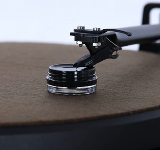 Kit di regolazione e pulizia Enova HIFI GVS 20, vista ravvicinata di una testina per giradischi su un supporto circolare nero e trasparente, piatto marrone sullo sfondo