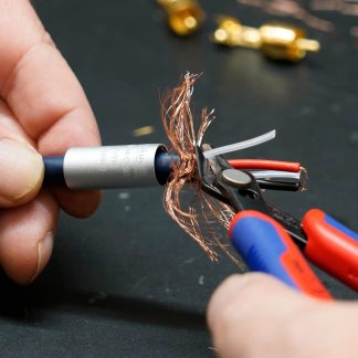 Tæt sidebillede af en metaltrådskærer med blå og røde håndtag, der skærer kobberfletningen på et blåt kabel med en cylindrisk sølvfarvet ring