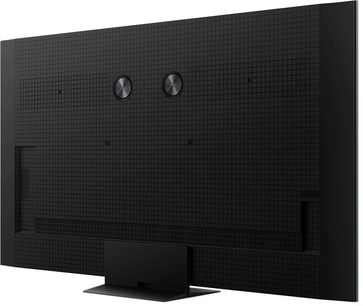 Televisor de alta definición TCL 85C9K negro, con chasis de plástico mate texturizado, equipado con dos discos circulares metalizados y una base central rectangular de metal, vista trasera lateral derecha