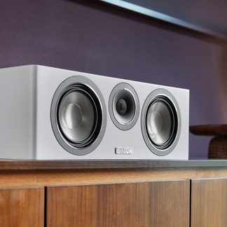 Cassa centrale hi-fi Canton bianca con tre altoparlanti circolari, appoggiata su mobile TV in legno