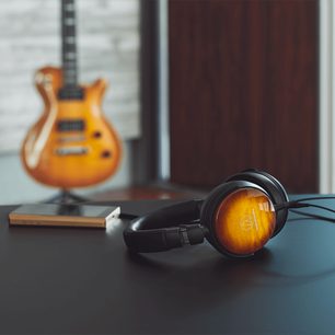 Lukket Audio-Technica ATH-WP900 hovedtelefon i træ, placeret på en bog, med en uskarp orange elektrisk guitar i baggrunden