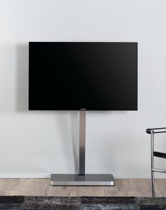 Moderne TV-møbel i mørkt gråt metal og glas, med integreret holder til fladskærm, placeret på et lyst trægulv