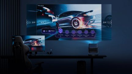 Cameră întunecată, ecran gigant cu mașină în mișcare, proiector pe masă, scaun de gaming, ecran de computer, tastatură