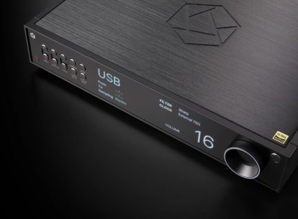 Juodo garso įrenginio vaizdas iš kampo su mygtukais, ekranu, kuriame rodoma "USB" ir "16", reljefiniu logotipu, apvaliu garso reguliavimo mygtuku.