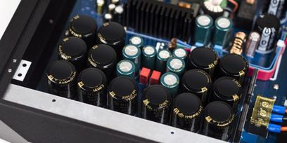 Nærbillede af bagsiden af en sort Nuprime Evolution One effektforstærker med mange elektrolytiske kondensatorer og stik