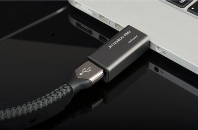 Bærbar Audioquest Jitter Bug FMJ sort lydkonverter, tilsluttet en sølvfarvet bærbar computer via et sort flettet USB-kabel