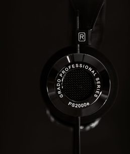 Åben hi-fi hovedtelefon Grado PS2000e, tæt forfra-udsigt på sort baggrund, rund perforeret metalrist på højre ørekop med R-logoet