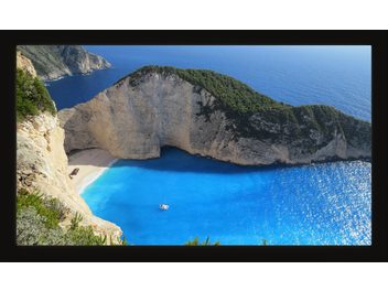 Plage de sable et rochers surplombée par des falaises escarpées couvertes de végétation, avec une crique d'eau turquoise