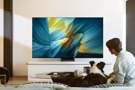 Televisore con cornice ultrasottile in metallo nero, schermo lucido che mostra un motivo astratto blu-verde e giallo, posizionato su un supporto centrale nero, vista frontale